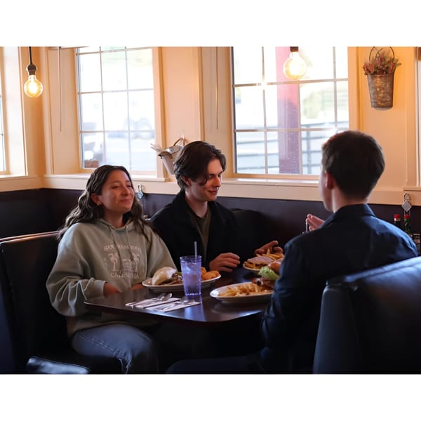 Three young people enjoying breakfast and conversation in a cozy booth at Waffle Shop.