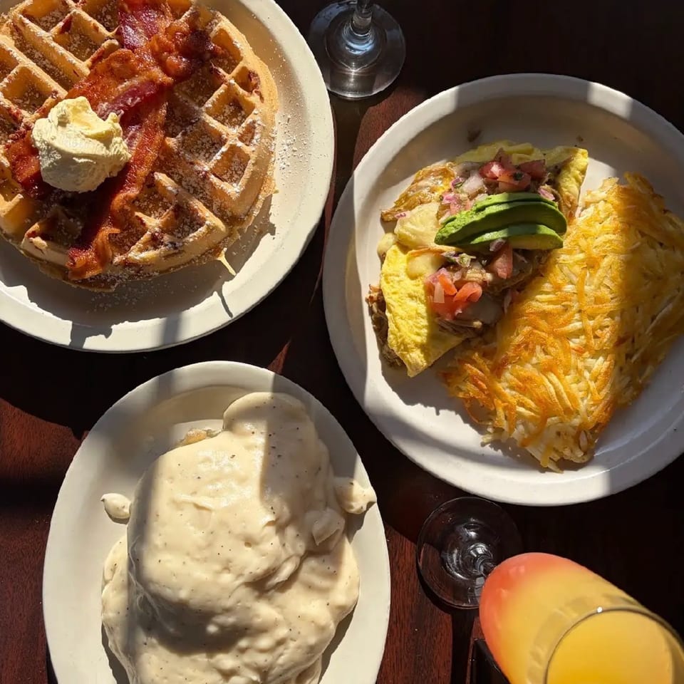 Three breakfast plates: waffles with bacon, omelet with hash browns, and biscuits with gravy.