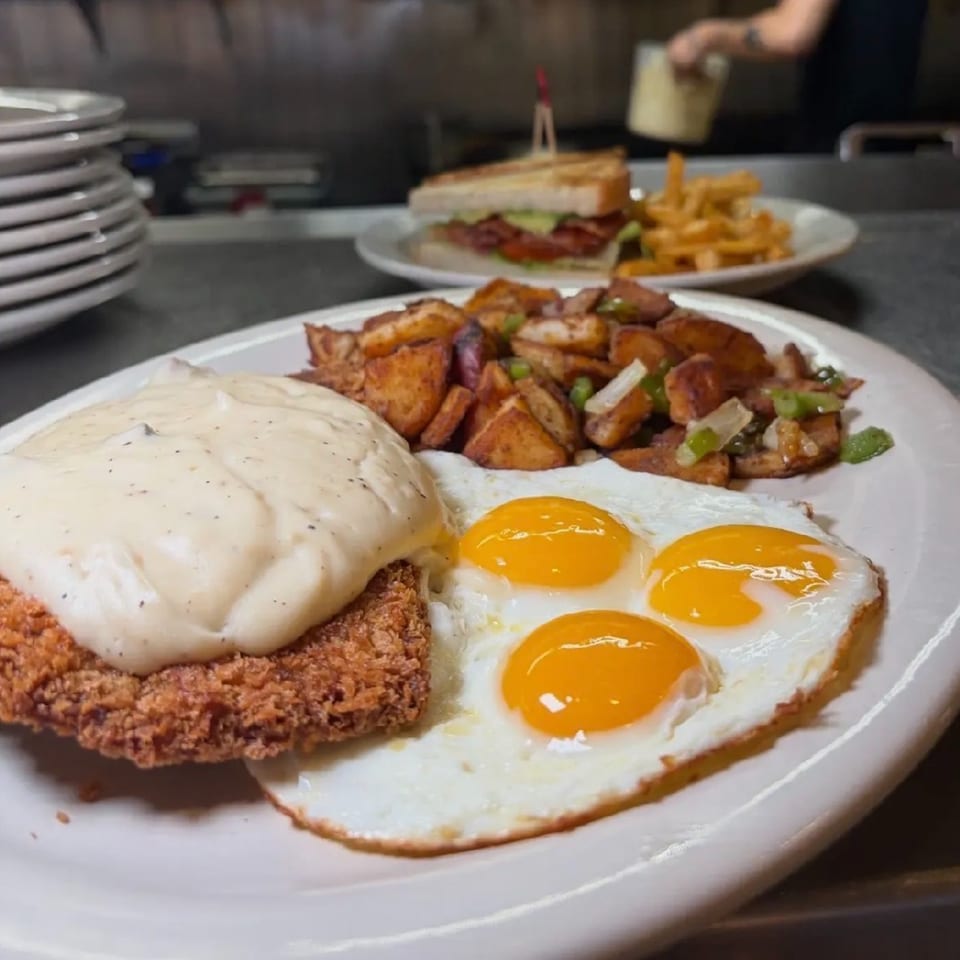 Chicken fried steak with gravy, three sunny-side-up eggs, and home fries on a white plate.