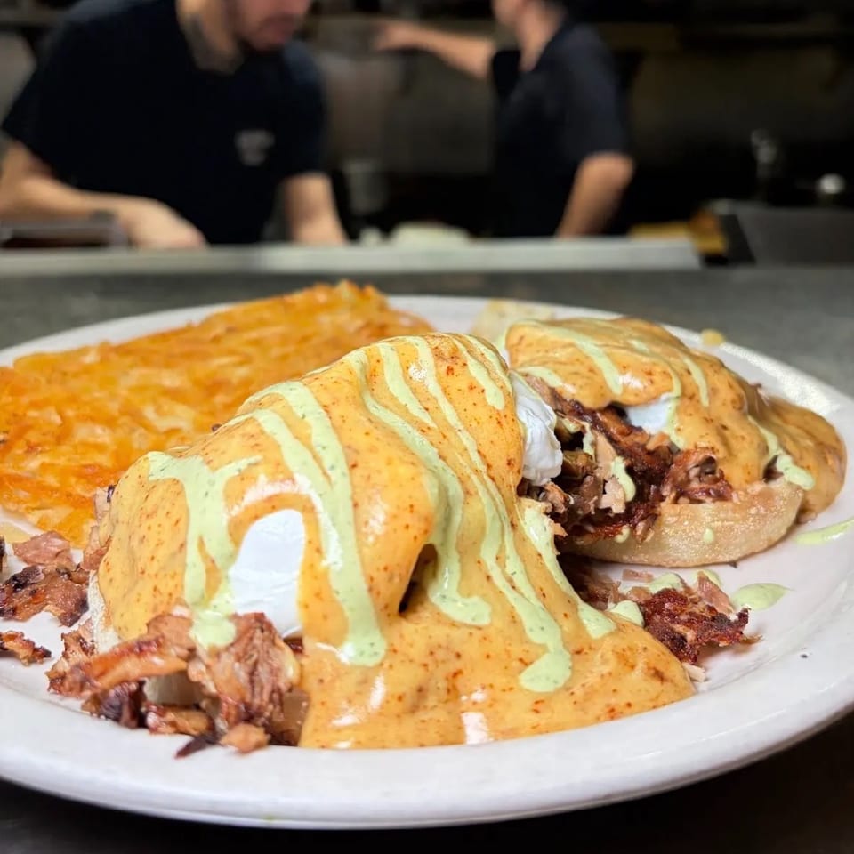 Two eggs benedict with pulled pork, hollandaise, and green sauce, served with hash browns.