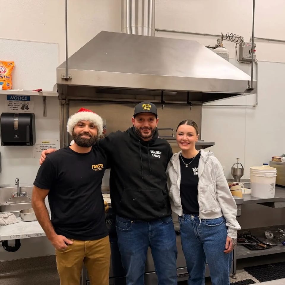 Three smiling Waffle Shop employees, two men and one woman, stand together in a commercial kitchen.