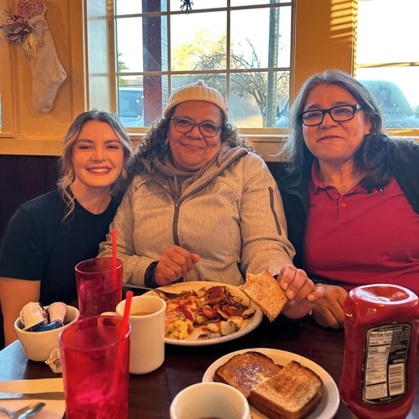 Three women smiling at the Waffle Shop, enjoying breakfast with omelets, potatoes, and toast.