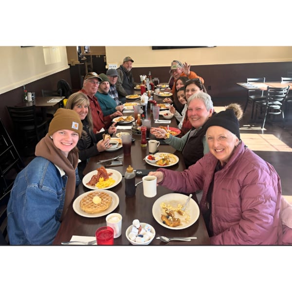 Smiling customers enjoying breakfast waffles, bacon, and eggs at Waffle Shop.