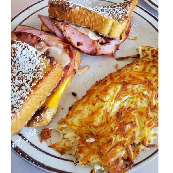 A breakfast plate with two French toast sandwiches filled with ham and cheese, alongside crispy hash browns.
