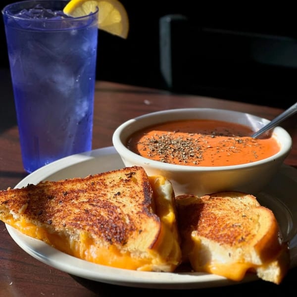 Grilled cheese sandwich with tomato soup and a blue drink with a lemon slice.
