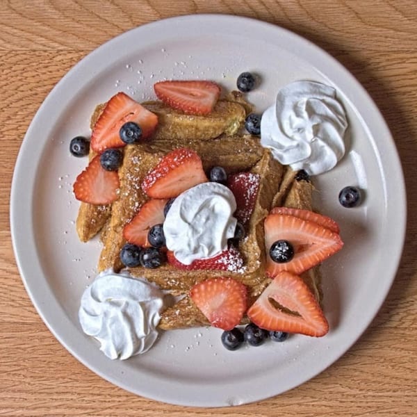 Golden waffles from Waffle Shop, topped with fresh strawberries, blueberries, whipped cream, and powdered sugar.