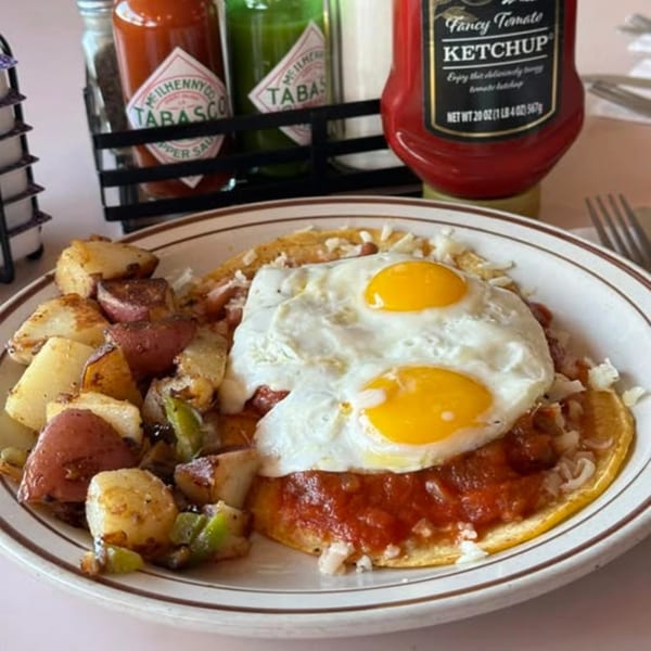 Breakfast plate with two fried eggs, salsa, home fries, and Tabasco and ketchup bottles.